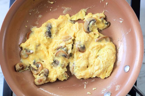 scrambled eggs with mushrooms and cheese in a copper pan