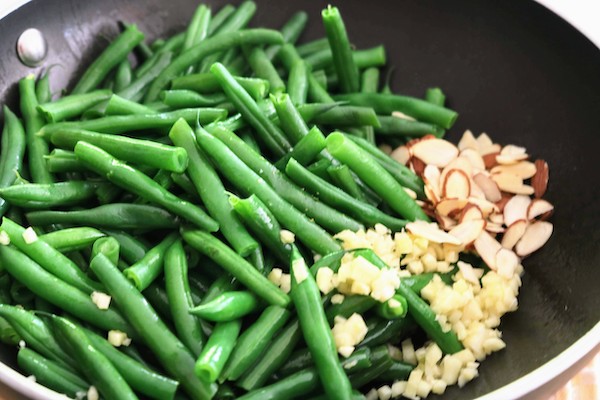 green beans in wok with chopped garlic and almonds